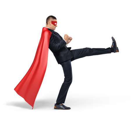 A businessman in a red superhero cape kicking an invisible object on white background.の写真素材