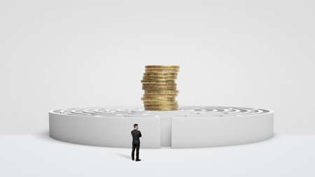 A tiny businessman standing in front of a white round maze with a stack of giant coins on the maze walls.の写真素材