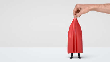 A giant hand taking off a red drapery from a hidden businessman on white background.の写真素材