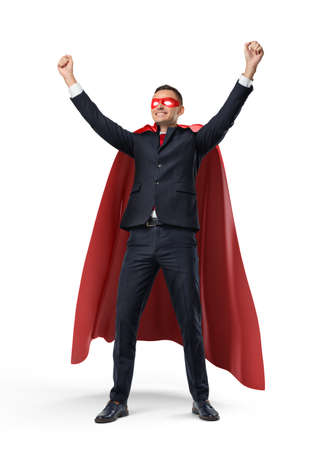 A businessman in a superhero red cape and a mask standing in front view with hands raised in victory on white background.の写真素材