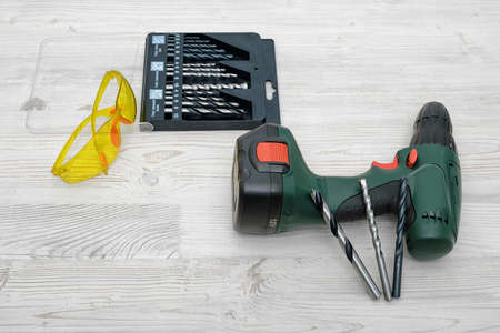 A cordless drill set on a wooden table background with a set of bits in the box and yellow...