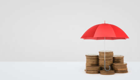 A red open umbrella vertically placed over several stacks of golden coins on white background.の写真素材