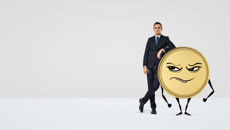 A businessman leaning on a golden coin with arms, legs and a grumpy face.の写真素材