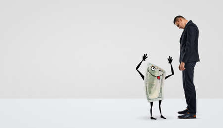 A businessman looking down at a humanoid dollar bill that makes faces.の写真素材