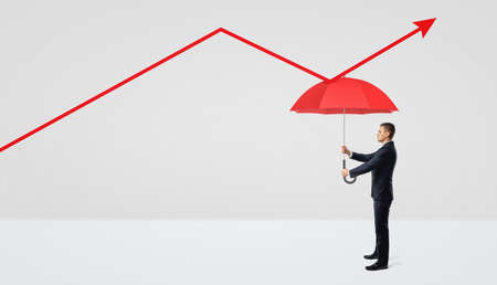 A businessman holding a red open umbrella right under a red statistic arrow pointing upwards.の写真素材