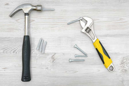 A silver hammer, a wrench, several screw bolts and dowels on light wooden background.の写真素材