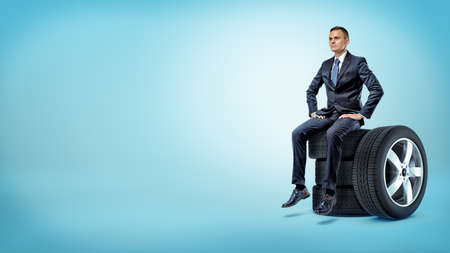A serious businessman sitting on a stack of car tires with hands on his hips.の写真素材