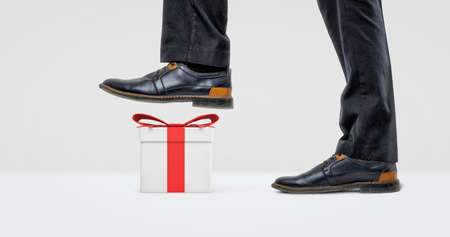 A giant businessman boot ready to step on a white gift box with a red bow.の写真素材
