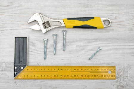 A yellow angle ruler, a wrench and four screw bolts placed on light wooden table.