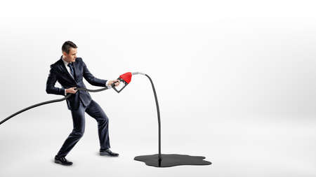 A businessman on white background holding a new red gas nozzle thats leaking oil to a large black puddle.の写真素材