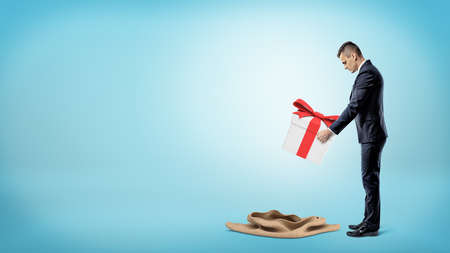 A businessman on blue background putting a large gift box into an empty sack.の写真素材