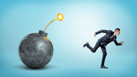 A small businessman on blue background running away from a giant bomb with a lit fuse.の写真素材