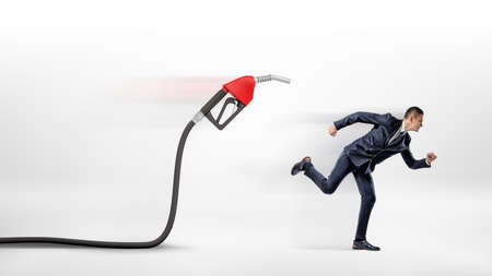 A businessman on white background running away from a red gas nozzle attached to a black hose.の写真素材
