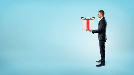 A businessman on blue background standing in side view and holding a gift box.