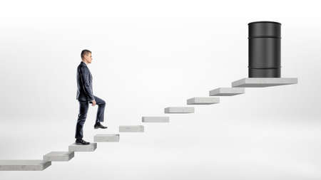 A businessman on white background walking up a concrete block stairs where a black oil barrel stands on the top.の写真素材