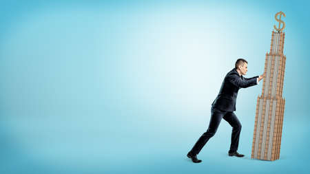 A large businessman pushing a sloping business building of the same height on blue background.の写真素材