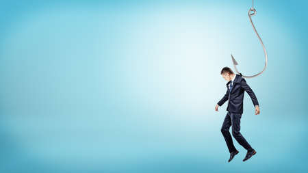 A tiny businessman hanging from a giant silver fishing hook like a puppet doll.の写真素材