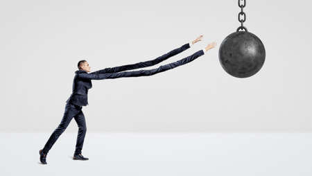 A businessman on white background trying to grab a wrecking ball with his extremely long arms.の写真素材