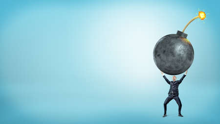 A tiny businessman holding a giant lit bomb in both hands.の写真素材