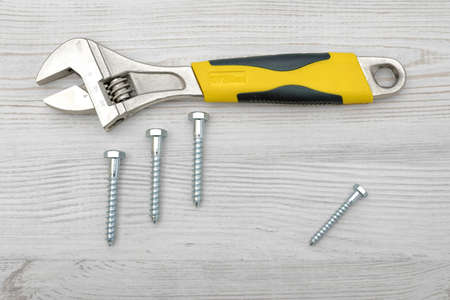 A yellow wrench and four screw bolts placed on light wooden table.の写真素材