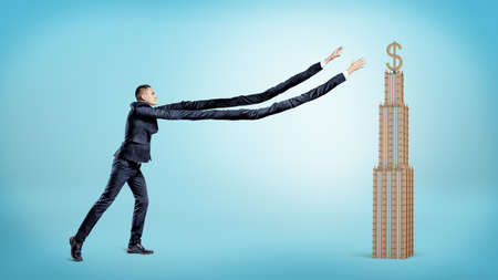 A businessman with extremely long arms trying to catch a small business building with a golden dollar sign on the top.の写真素材