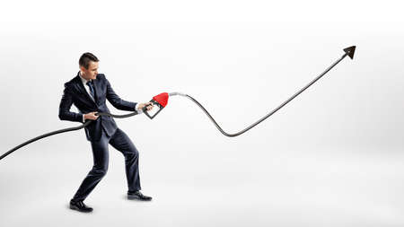 A businessman holds a gas pump nozzle which shots out oil into a black raising line with an upwards arrow.の写真素材