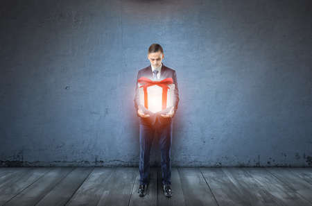 A businessman on dark blue background holds a large glowing giftbox.の写真素材