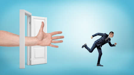 A giant open hand tries to catch a small running businessman through an open white door.の写真素材