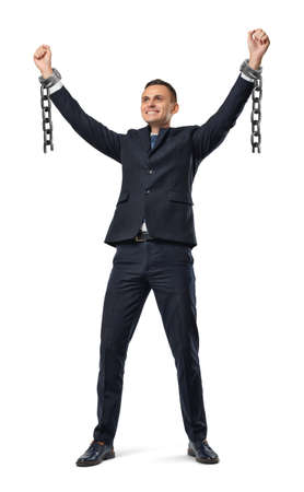 A happy businessman with hands raised up showing broken shackles on white background.の写真素材