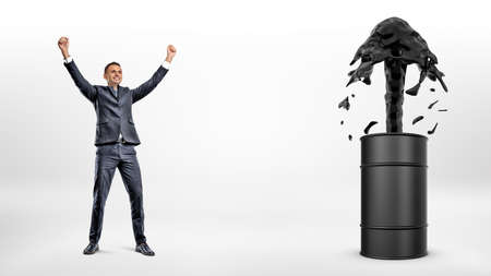 A happy businessman beside a black barrel with a strong current of oil flowing out of it.の写真素材