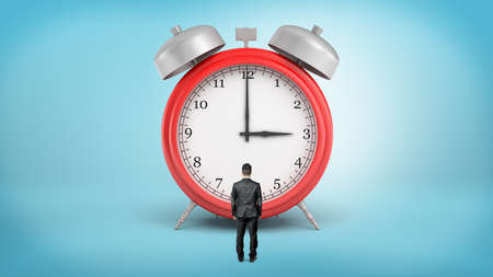 A tiny businessman with his back turned stands in front of a giant red alarm clock.
