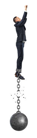 A businessman jumps in the air while connected to a large iron ball with a broken chain.の写真素材