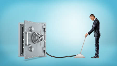 A businessman holds a lever connected with a black hose to an open safe box.の写真素材