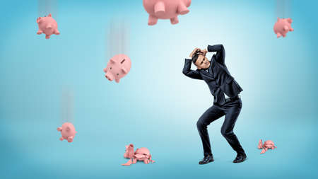 A businessman hides his head from many piggy banks that fall down and crack at the floor.の写真素材