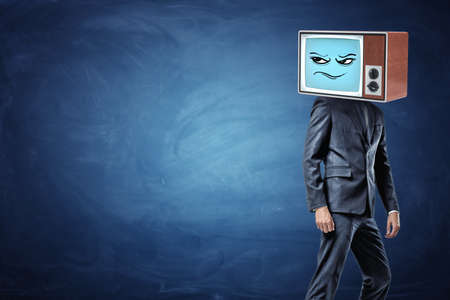 A businessman stands half-turned and ready to leave while wearing an old TV with a sceptic emoticon on his head.の写真素材