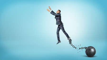 A businessman leaps up with outstretched hands while hes chained to an iron ball with a broken link.の写真素材