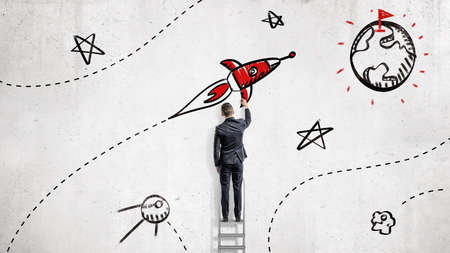 A businessman draws paints a rocket that will reach a goal set on a planets surface.の写真素材