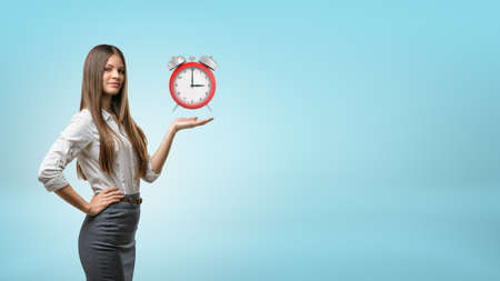 A blond businesswoman stands and holds one hand palm up with red retro alarm clock hovering above it.の写真素材