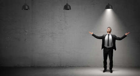 A businessman stands on concrete background under the light of a single working industrial lamp.の写真素材