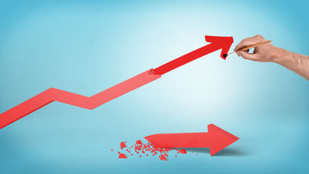 A male hand draws a new point for a red statistic arrow instead of a broken and a fallen one.の写真素材