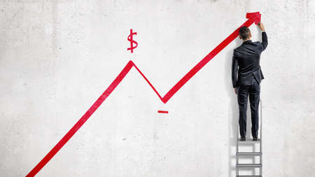 A businessman stands on a step ladder and draws a red statistic arrow moving up with a dollar sign.の写真素材