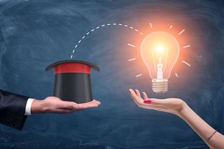 3d rendering of a male businessmans hand holding a wizards hat and a female hand holding a bright glowing lamp.の写真素材