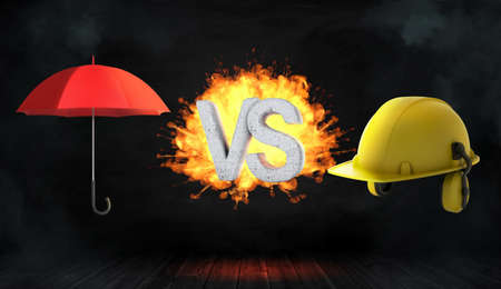 3d rendering of large letters VS on fire stand between an open red umbrella and a large yellow construction helmet.の写真素材