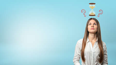 A portrait of a thinking businesswoman with a small hourglass and question marks above her head.の写真素材