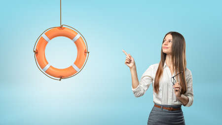 A long-haired businesswoman points to a small orange life buoy hanging from a rope.の写真素材