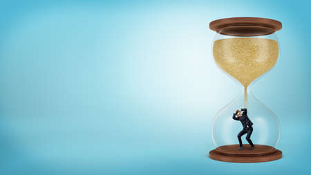 A tiny businessman stands inside a hourglass when the sand only starts to fall over him.の写真素材