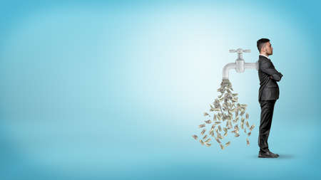 A businessman stands in a side view with a large faucet attached to his back and leaking money bills.の写真素材