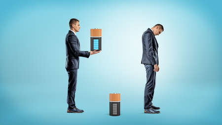 A businessman brings a large fully charged battery to replace a depleted one from inside a very tired businessman.の写真素材