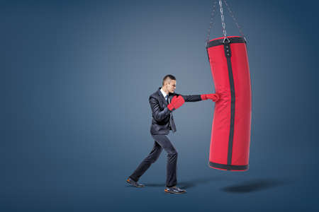 A businessman in red sports gloves hits a giant red and black boxing bag.の写真素材