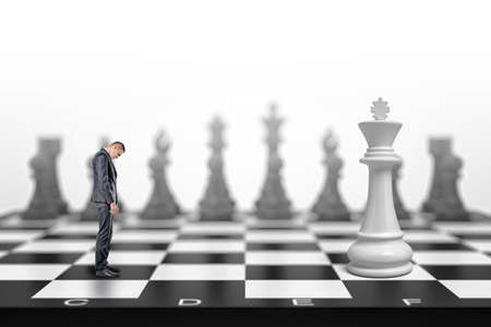 A small businessman stands with his head down in front of a white kind on a large chessboard.の写真素材